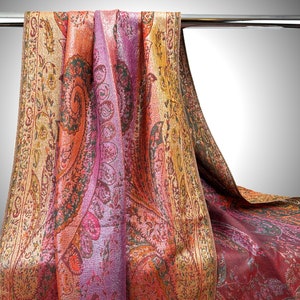 May include: A long, rectangular shawl with a paisley pattern in shades of gold, orange, pink, and purple. The shawl is draped over a silver bar.