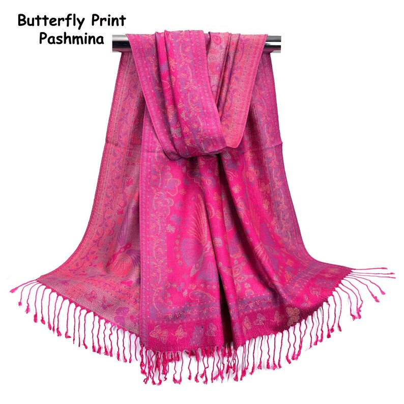 May include: A bright pink pashmina featuring a butterfly print and intricate floral patterns. The scarf has a rectangular shape with fringed edges at the bottom. The text "Butterfly Print Pashmina" is visible in the upper left corner.