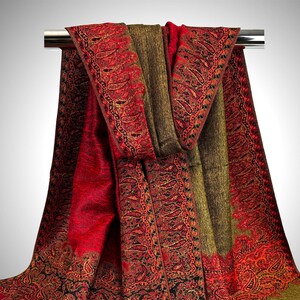 Pode incluir: Um xale vermelho e verde com padr&atilde;o paisley e borda franjada. O xale est&aacute; drapeado sobre uma barra de metal.