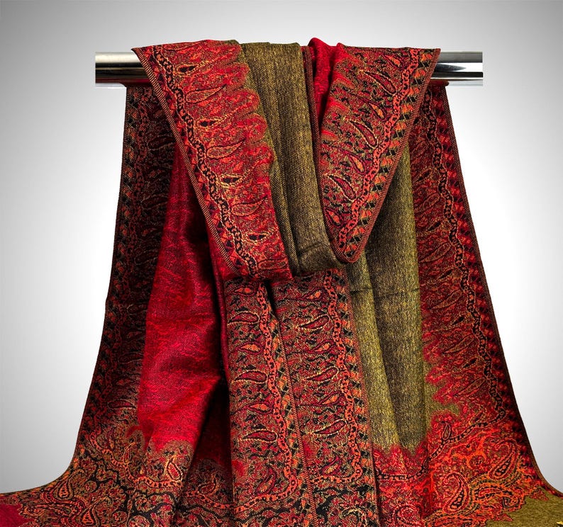 Pode incluir: Um xale vermelho e verde com padr&atilde;o paisley e borda franjada. O xale est&aacute; drapeado sobre uma barra de metal.