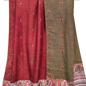 K&ouml;nnte beinhalten: Ein roter und olivgr&uuml;ner Schal mit gestickten Blumenmustern. Der Schal hat einen detaillierten Rand mit Paisley- und geometrischen Designs. Der Stoff ist &uuml;ber einer Metallstange drapiert und zeigt die Textur und Farbvariationen.