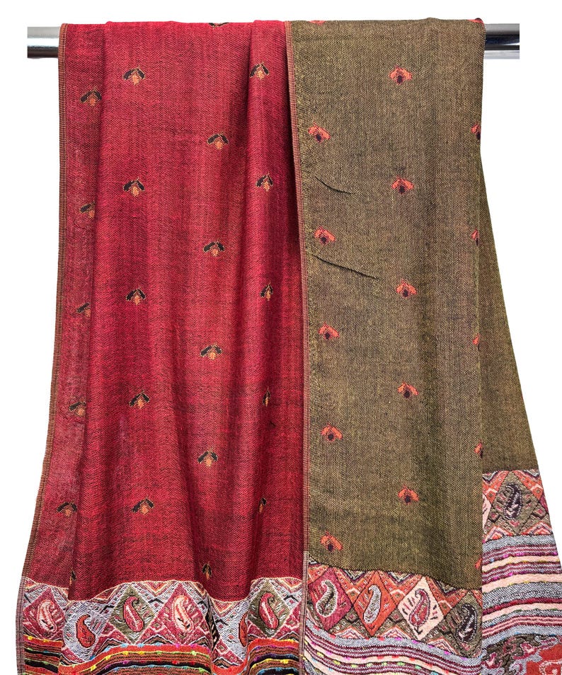 K&ouml;nnte beinhalten: Ein roter und olivgr&uuml;ner Schal mit gestickten Blumenmustern. Der Schal hat einen detaillierten Rand mit Paisley- und geometrischen Designs. Der Stoff ist &uuml;ber einer Metallstange drapiert und zeigt die Textur und Farbvariationen.