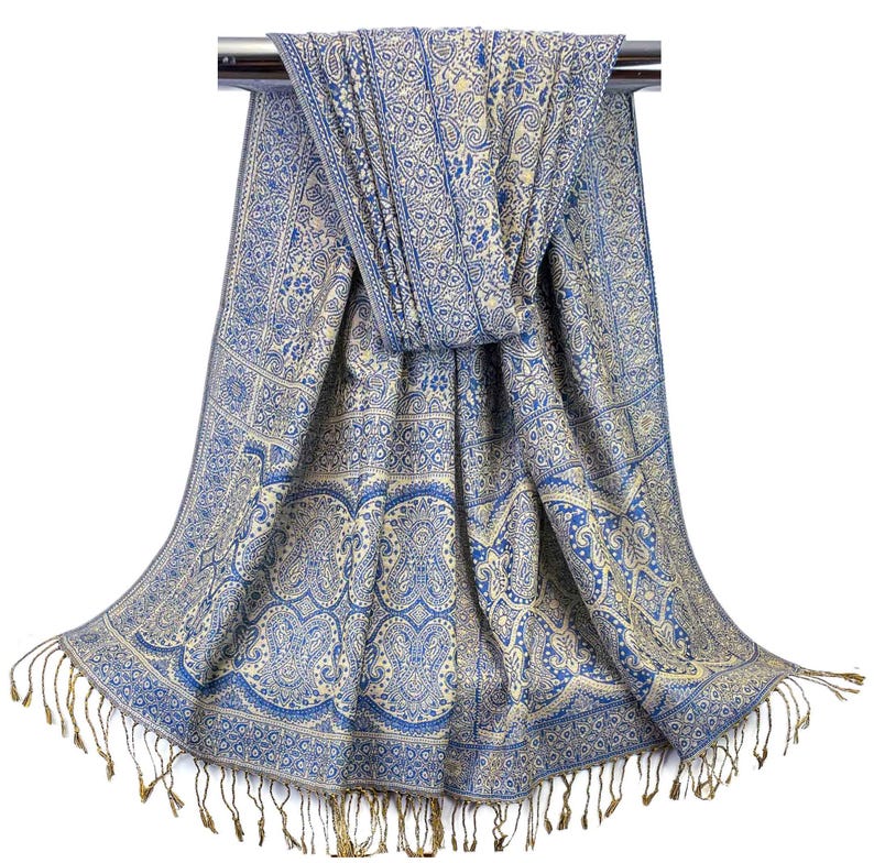 May include: A blue and cream paisley patterned scarf with gold fringe. The scarf is draped over a silver rod.