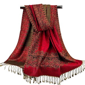 Pode incluir: Um cachecol vermelho e marrom com padr&atilde;o paisley e franjas douradas. O cachecol est&aacute; drapeado sobre uma haste prateada.