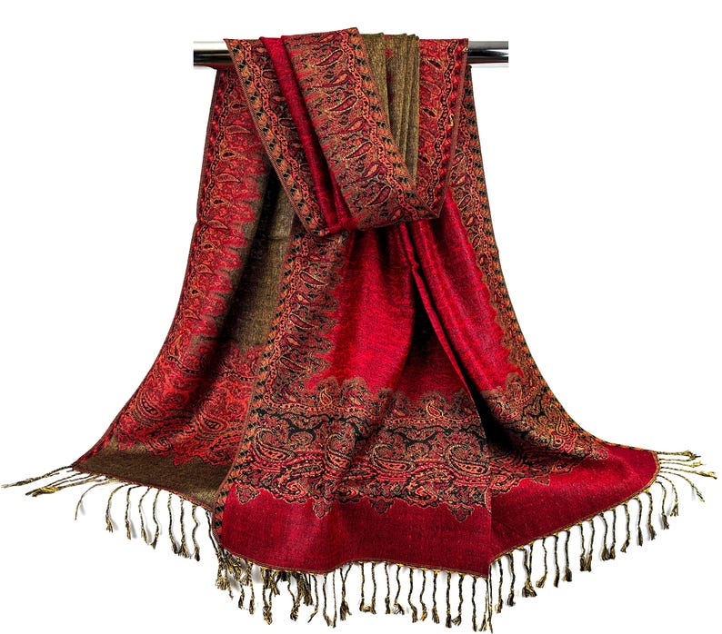 Pode incluir: Um cachecol vermelho e marrom com padr&atilde;o paisley e franjas douradas. O cachecol est&aacute; drapeado sobre uma haste prateada.
