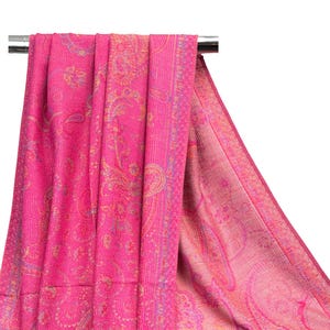 May include: A vibrant fuchsia pink shawl featuring an intricate woven paisley pattern in shades of gold and light blue. The fabric displays a dense, textured weave with a wide decorative border along the edge, showcasing a repeating floral motif.