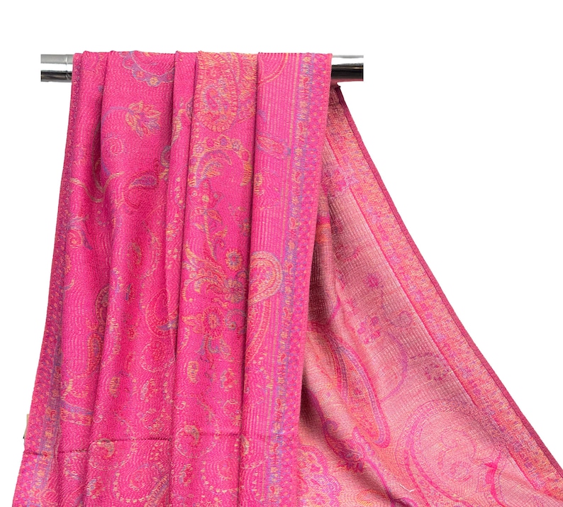 May include: A vibrant fuchsia pink shawl featuring an intricate woven paisley pattern in shades of gold and light blue. The fabric displays a dense, textured weave with a wide decorative border along the edge, showcasing a repeating floral motif.