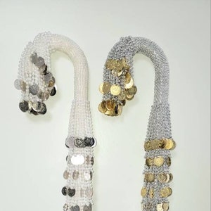 May include: Two decorative wands with a silver and gold coin design. The wands are made of beads and have a curved handle.