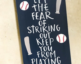Puede incluir: Un letrero de madera azul oscuro con letras blancas y costuras de béisbol rojas. El letrero dice "Nunca dejes que el miedo a poncharte te impida jugar el juego - Babe Ruth".