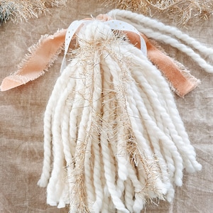 Peut inclure: Ornement en forme d'ange fait à la main, avec un corps en fil blanc et des accents de tinsel doré. L'ange a des ailes en tissu pêche et un ruban blanc à pois dorés. Pour la décoration festive ou saisonnière.
