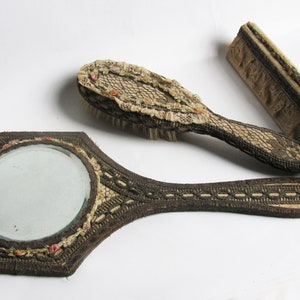 Puede incluir: Un conjunto de tocador vintage con un espejo de mano, un cepillo para el cabello y un peine. El conjunto está decorado con encaje y bordado.