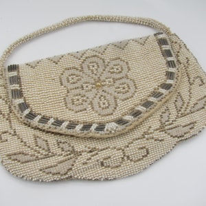 May include: A white beaded evening bag with a floral design and a silver trim. The bag has a flap closure and a top handle.