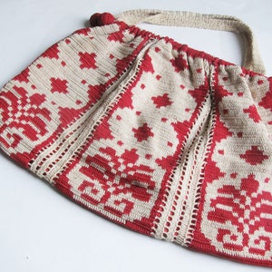 May include: A crocheted bag with a white and red geometric pattern. The bag has a long strap and a drawstring closure.