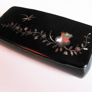 May include: A black rectangular box with a floral design made of mother of pearl. The design includes a flower, leaves, and a dragonfly.