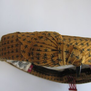 May include: A brown and black patterned headband with a bow on top. The headband is made of a soft, fabric material.
