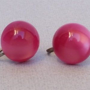 May include: A pair of pink clip-on earrings with a smooth, round, and slightly iridescent finish.