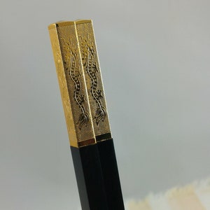May include: A pair of black chopsticks with gold dragon designs on the top. The chopsticks are made of wood and have a smooth finish.