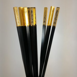 May include: A set of black chopsticks with gold tips. The tips are decorated with a dragon design.