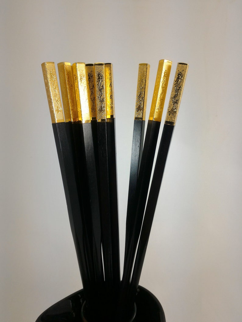 May include: A set of black chopsticks with gold tips. The tips are decorated with a dragon design.
