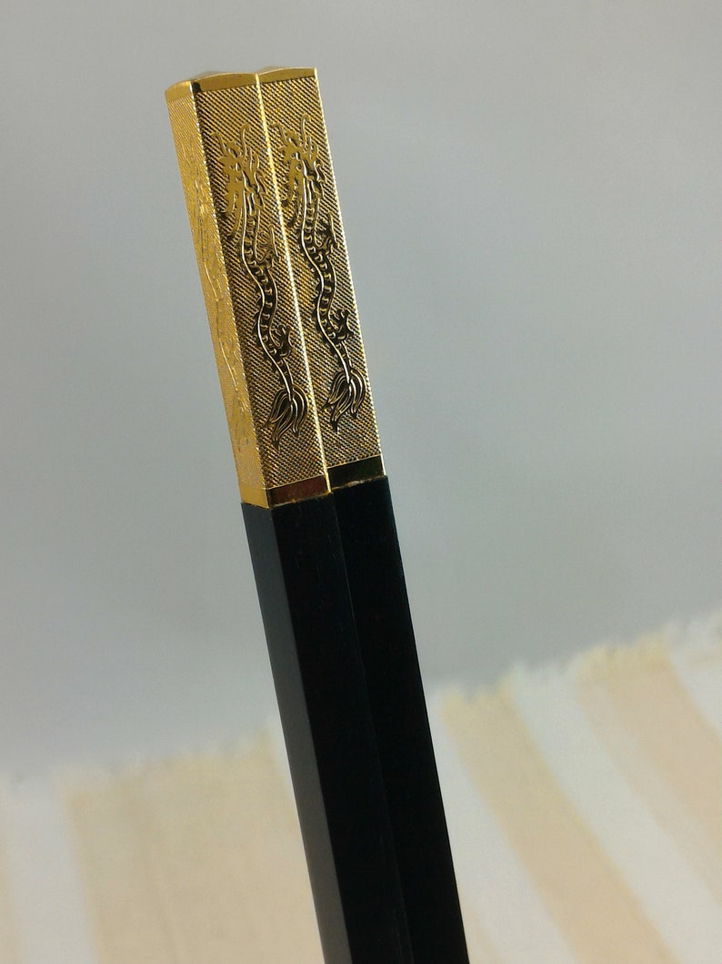 May include: A pair of black chopsticks with gold dragon designs on the top. The chopsticks are made of wood and have a smooth finish.
