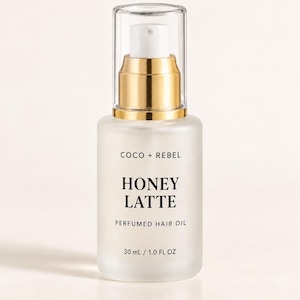 Peut inclure: Un flacon en verre dépoli d'huile capillaire parfumée Coco + Rebel Honey Latte avec une pompe dorée et un capuchon en plastique transparent. L'étiquette porte du texte noir et indique un volume de 30 ml pour ce produit de soin capillaire.