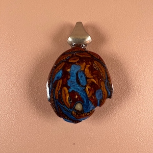 May include: A round pendant with a silver bail. The pendant is made of brown and blue resin with a swirling pattern.