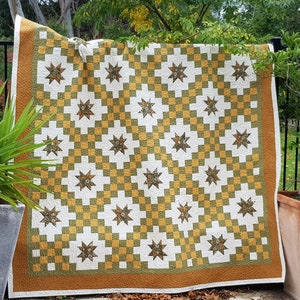 Könnte beinhalten: Eine große Steppdecke mit Patchwork-Muster, das ein sich wiederholendes Muster aus Sternen und Quadraten in Grün-, Gelb- und Weißtönen zeigt.