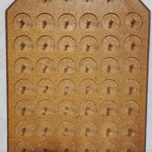 May include: A wooden pegboard with a light brown finish. The board has a series of evenly spaced holes with wooden pegs inserted. The top of the board is shaped like a house. The pegboard is likely used for a game or craft.