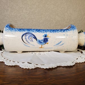 May include: A ceramic planter with a white speckled finish and blue accents. The planter features a hand-painted rooster design in blue and black. The planter is approximately 12 inches long.