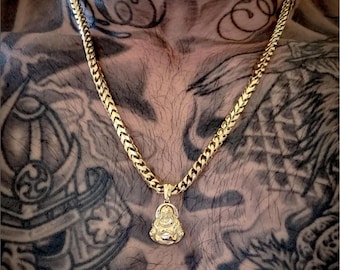 May include: A gold chain necklace with a small gold pendant shaped like a smiling Buddha. The necklace is worn by a person with tattoos on their chest.