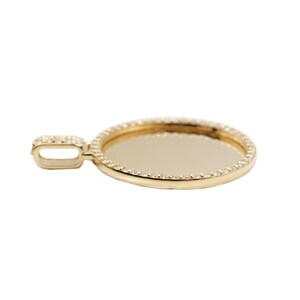 May include: A gold pendant with a round, clear, glass-like center surrounded by a border of small, clear stones.