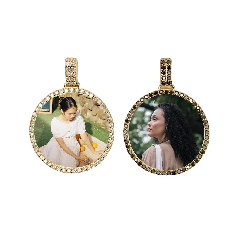 May include: Two gold pendants with a round photo frame. The frame is set with small diamonds. One pendant has a white diamond frame and the other has a black diamond frame.