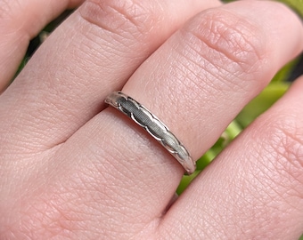 May include: A silver band ring with a textured design.