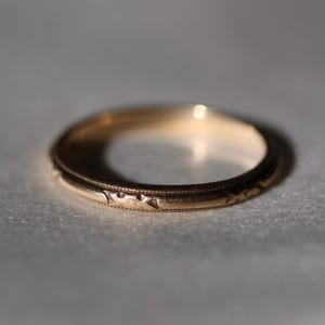 May include: A simple gold wedding band with a delicate engraved design.