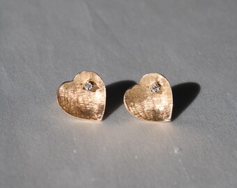 Puede incluir: Un par de pendientes de corazón de oro con un pequeño diamante en el centro de cada corazón.
