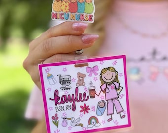 May include: A rectangular ID badge holder with a pink border featuring a cartoon nurse, a baby, a bottle, a teddy bear, a stork, and a rainbow. The text reads Kaylee BSN, RN. Above it is a smaller topper with five babies and the text NICU NURSE.