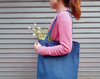 Puede incluir: Una mujer con un suéter rosa lleva una bolsa de mano azul con un ramo de flores blancas.