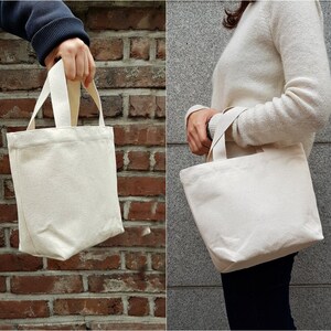 May include: Two white canvas tote bags with short handles. The bags are empty and appear to be made of natural cotton.
