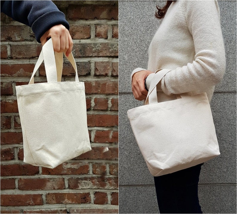 May include: Two white canvas tote bags with short handles. The bags are empty and appear to be made of natural cotton.