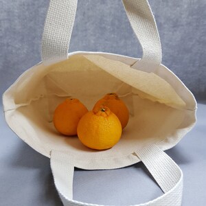 May include: A white canvas tote bag with three orange mandarins inside. The bag has two handles.