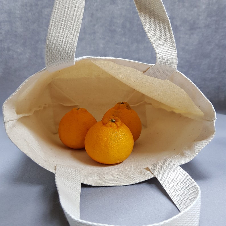 May include: A white canvas tote bag with three orange mandarins inside. The bag has two handles.