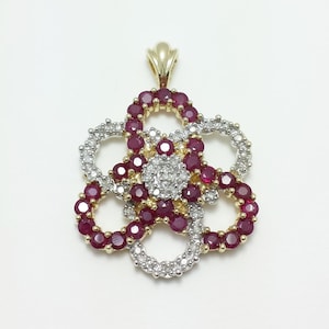 May include: A gold pendant necklace featuring a flower design with red rubies and white diamonds.