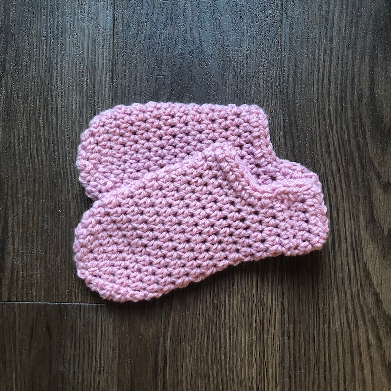 May include: A pair of crocheted slippers in a light pink color. The slippers are made with a simple stitch pattern and have a soft, cozy look.