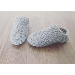 May include: A pair of gray crocheted slippers. The slippers are made with a simple stitch pattern and have a soft, cozy look.