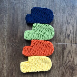 May include: Four crocheted slipper socks in different colors: blue, green, orange, and yellow. The socks are stacked on top of each other.