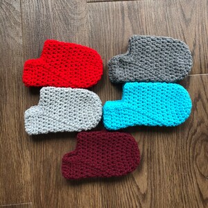 May include: Five crocheted slipper socks in different colors: red, gray, blue, maroon, and gray. The socks are all made with a similar stitch pattern.