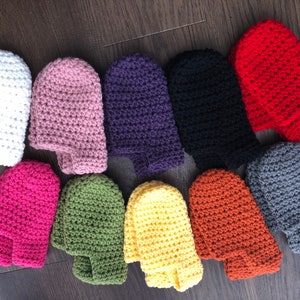 May include: A set of 10 crocheted fingerless gloves in various colors, including white, pink, purple, black, red, gray, green, yellow, and orange. The gloves are all made with a similar stitch pattern and are laid out in a row on a wooden surface.