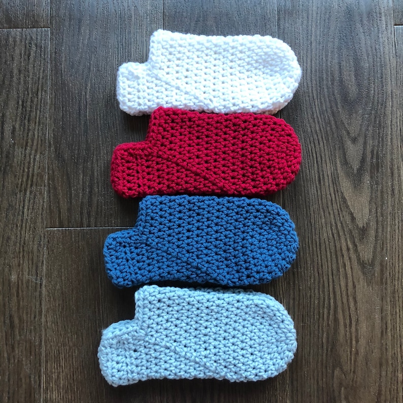 May include: Four crocheted slipper socks in different colors: white, red, blue, and light blue. The socks are stacked on top of each other on a wooden surface.