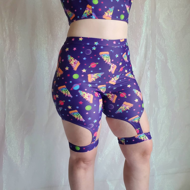 Puede incluir: Shorts morados y negros con estampado de pizza arco&iacute;ris y planetas. Los shorts tienen un dise&ntilde;o de corte en el muslo.