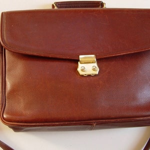 May include: A brown leather briefcase with a gold clasp and a long adjustable strap.